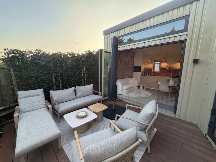 Terras met loungeset voor de open harmonicadeuren, bij zonsondergang